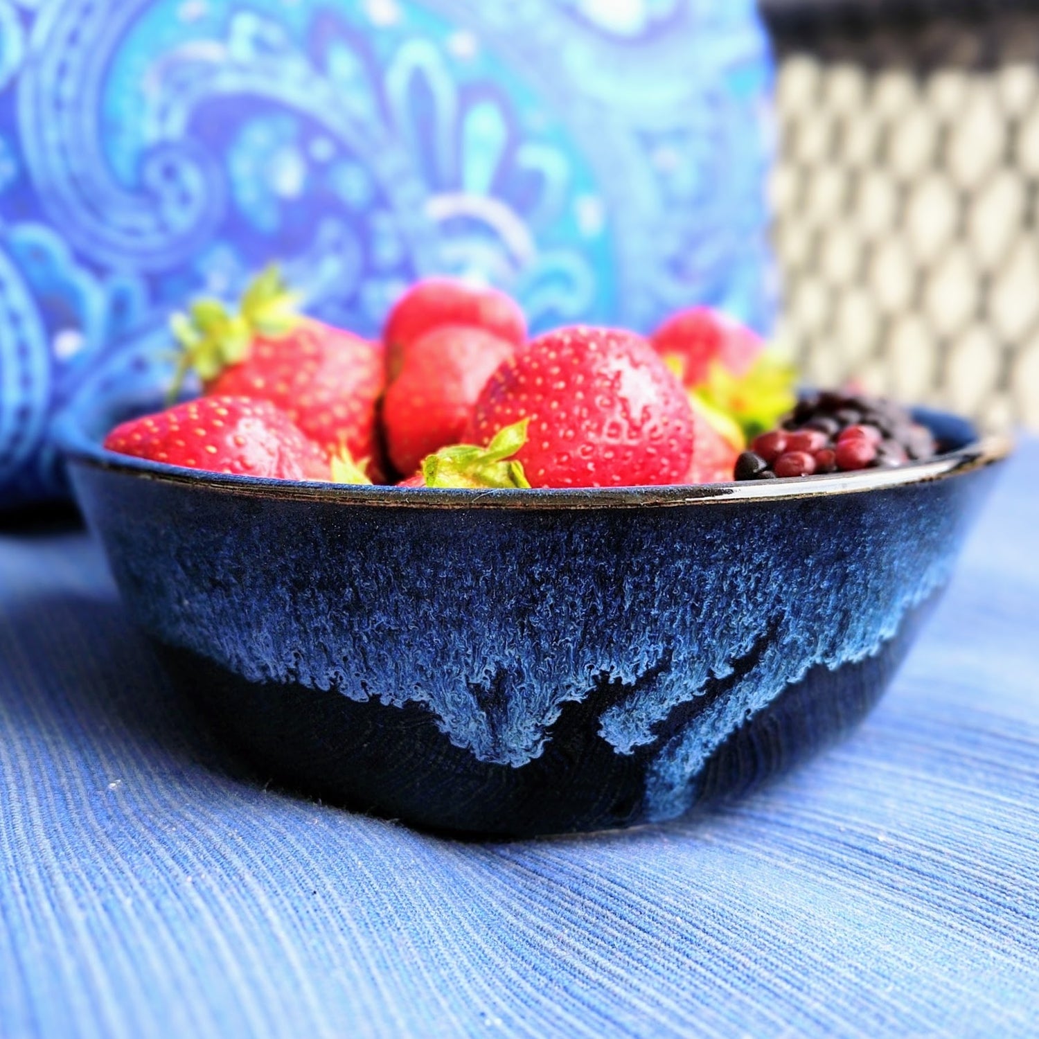 Lucious strawberries and blueberries in a handmade blue and black bowl sitting on a blue cushion